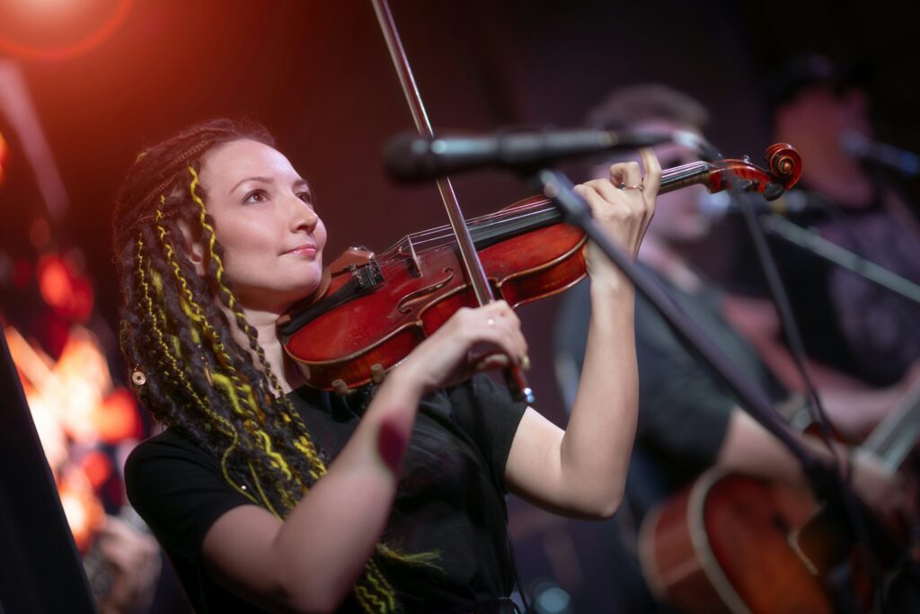 A female violinist plays the violin. Band performs on stage, rock music concert.