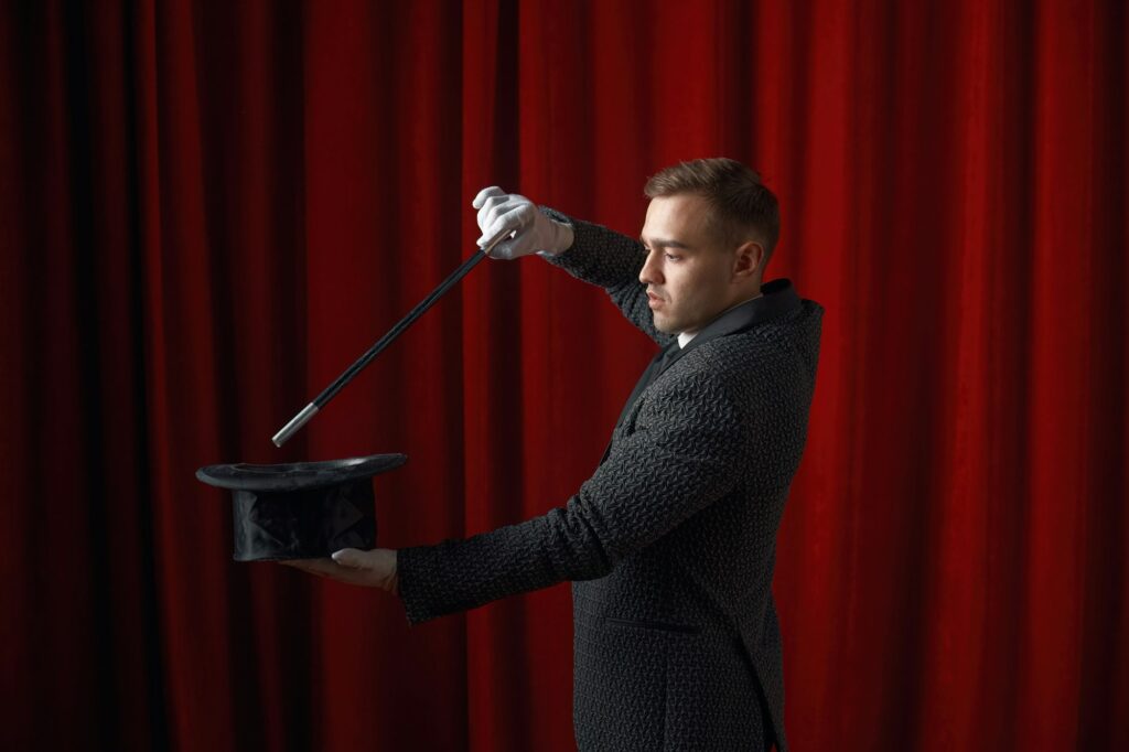 Young handsome illusionist performing magical trick with wand and hat